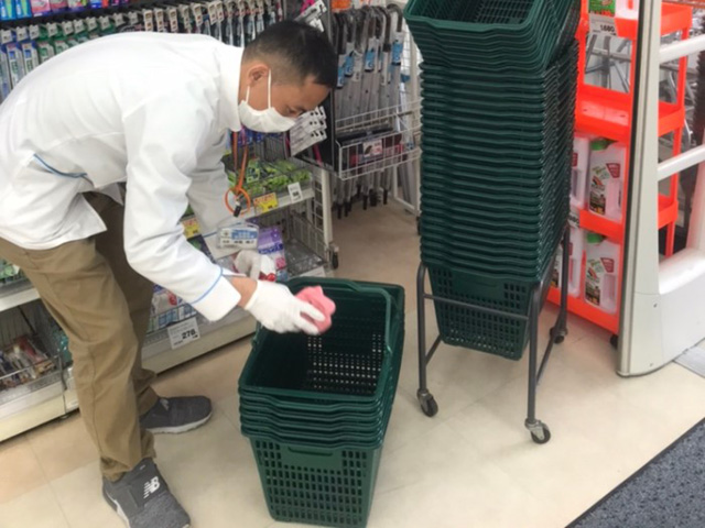 写真：買い物かごを消毒している従業員