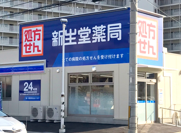 写真:24時間営業している新生堂薬局の外観。青地に白い文字で「24時間」と書かれた看板が壁に貼ってある。